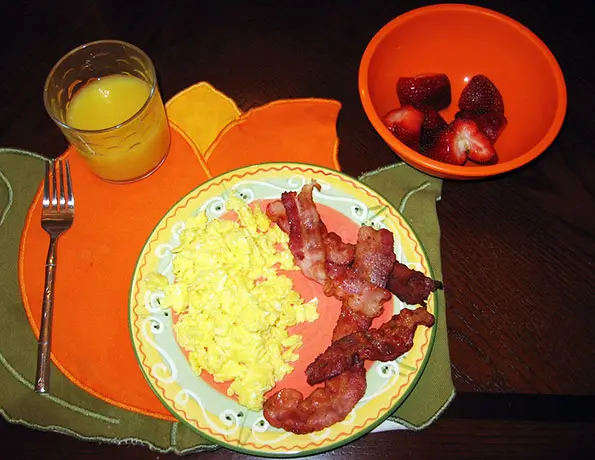 Un piatto con uova e pancetta, succo d'arancia in un bicchiere e fragole
