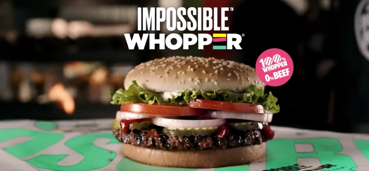 Un hamburger con pomodori e cipolle su un tavolo, e la scritta Impossible Whopper in cima