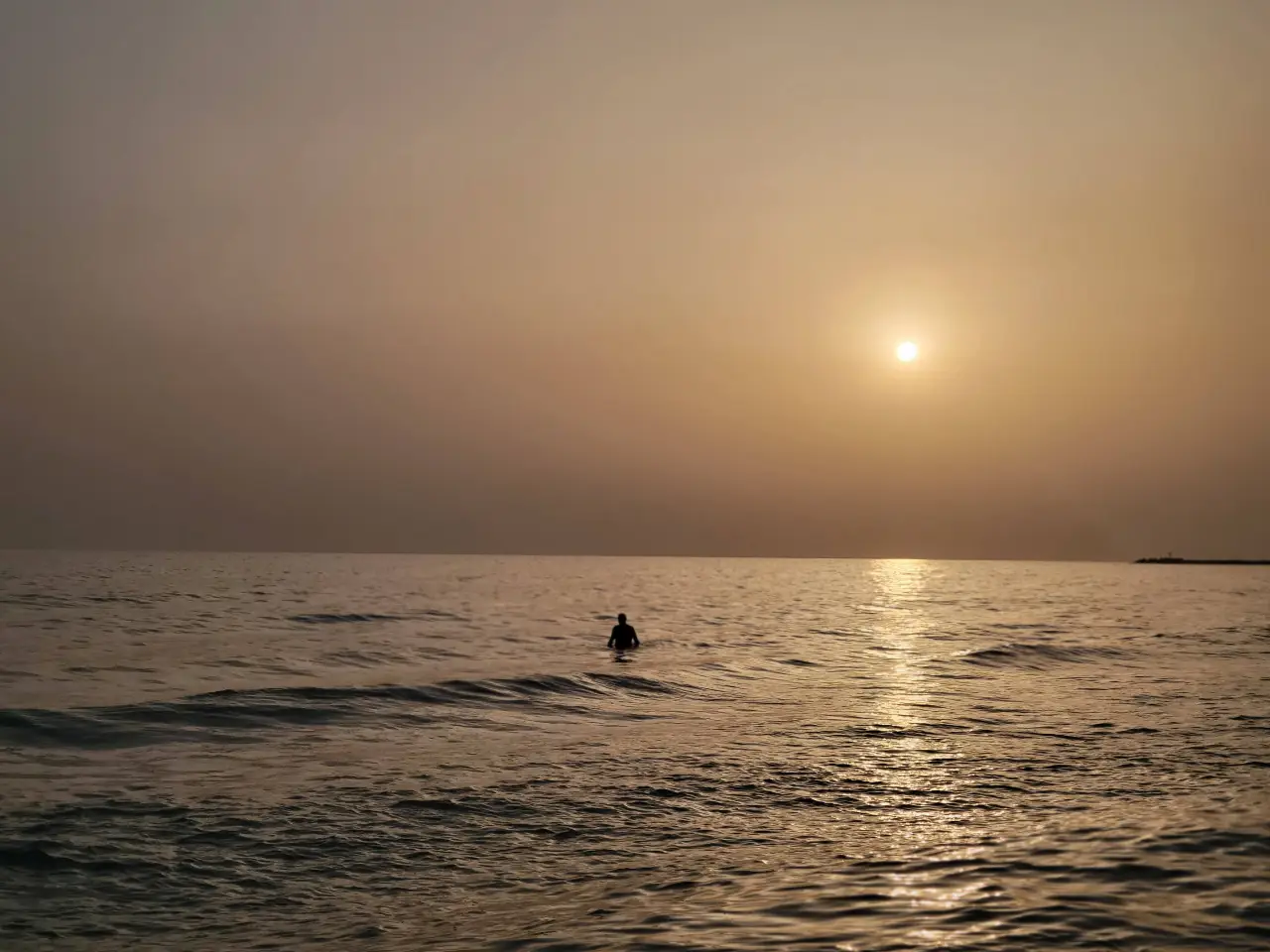 Un tramonto in riva al mare con una persona che si fa il bagno