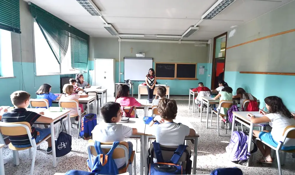 Studenti in una classe ascoltano l'insegnante appoggiata alla cattedra