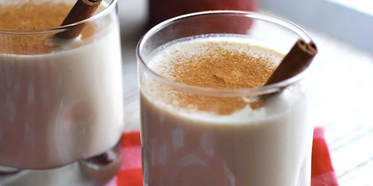 Due bicchieri pieni di coquito con bastoncini di cannella ed una spolverata di cannella