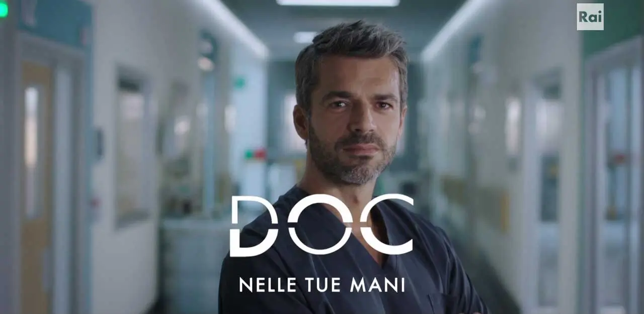 Il protagonista a mezzo busto con il camice scuro che guarda verso la telecamera