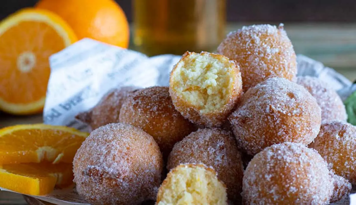Una manciata di zeppole sferiche su un piatto con delle fette di arance