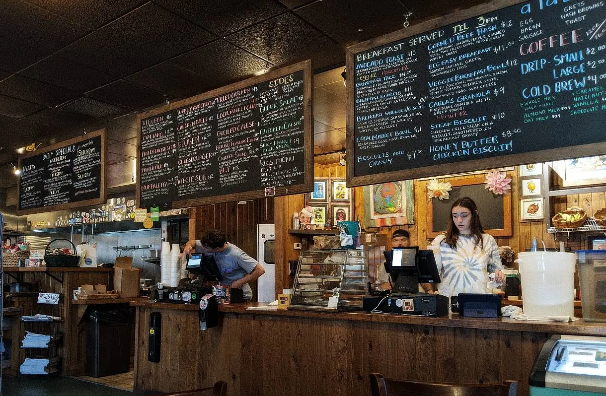 Il bancone di un locale con tutto il menu scritto su lavagne appese ad un muro