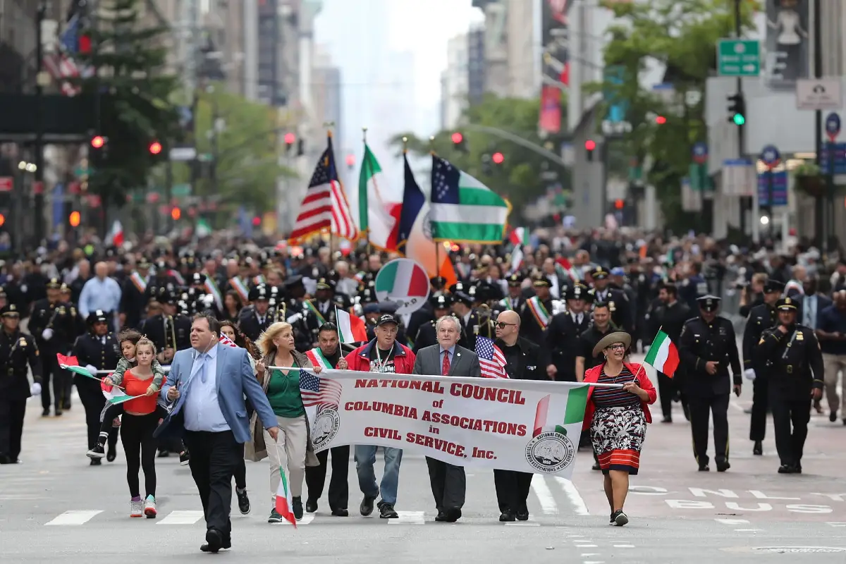 Una folta processione di persone con bandiere italiane ed americane
