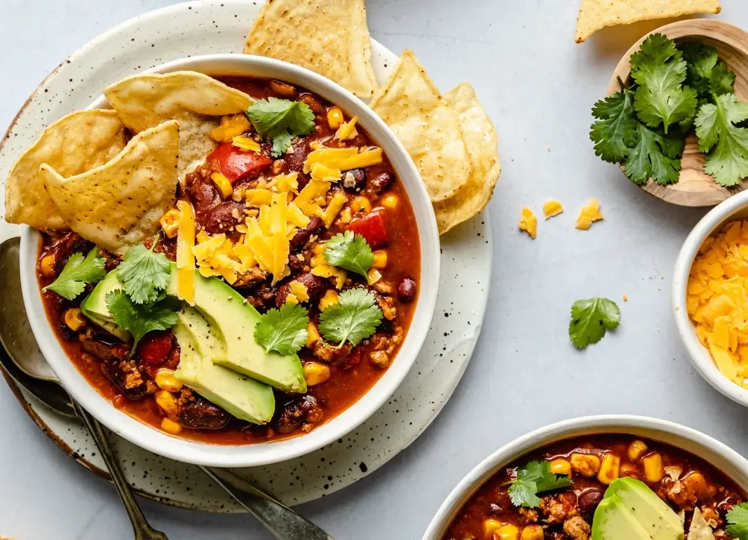 Un piatto rustico con chili, avocado, formaggio e due patatine per contorno