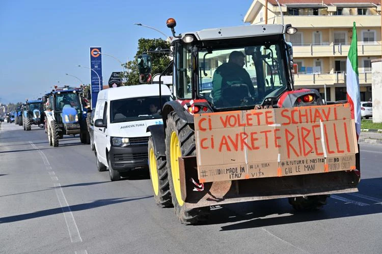 Trattori bloccano una strada di periferia. Su uno di essi un cartello dice: ci volete schiavi, ci avrete ribelli!