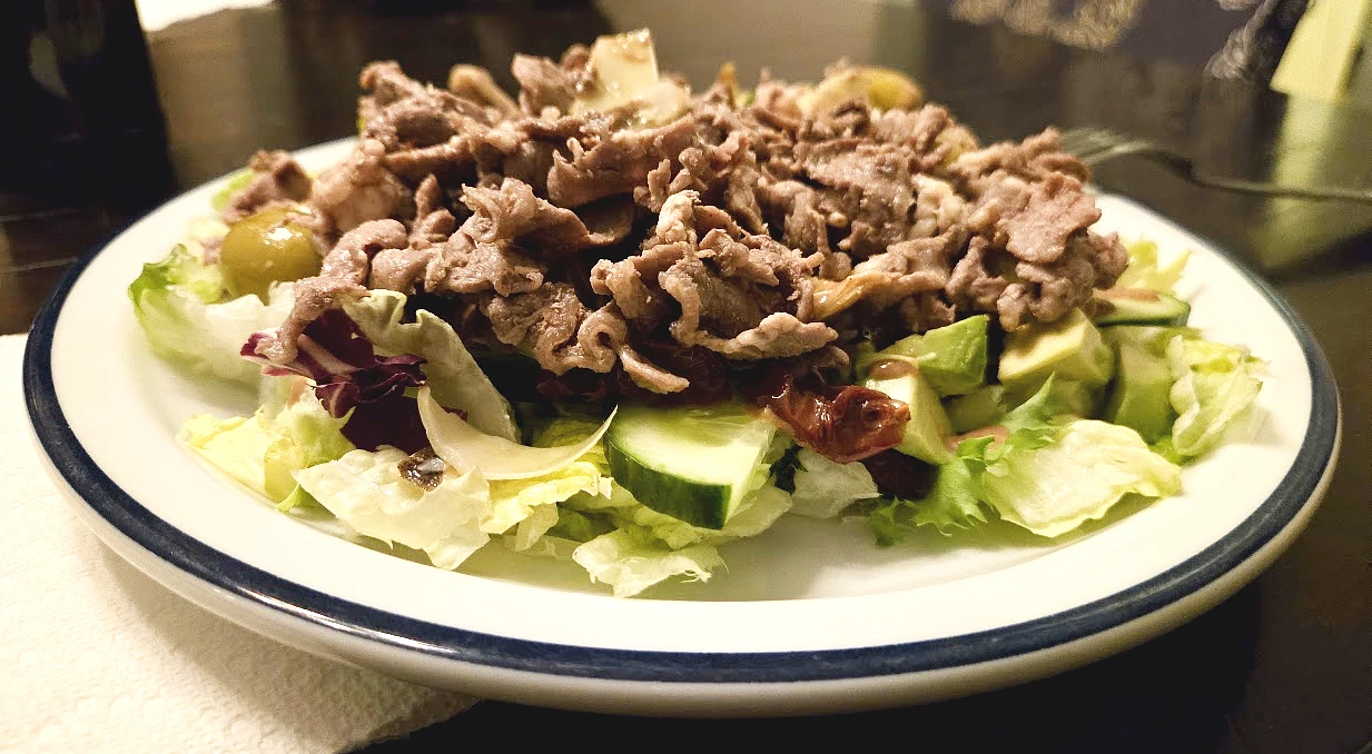 Carne, insalata, cetrioli, pomodorini, olive ed altri ingredienti in un piatto