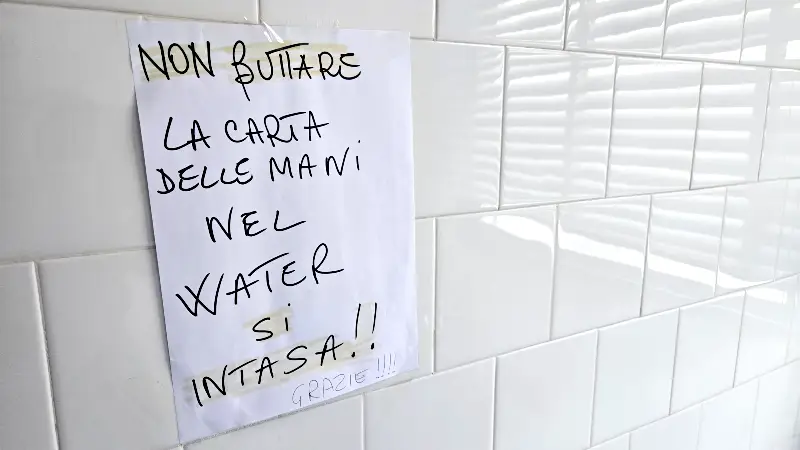 Un foglio su un muro recita: Non buttare la carta delle mani nel water, si intasa!!